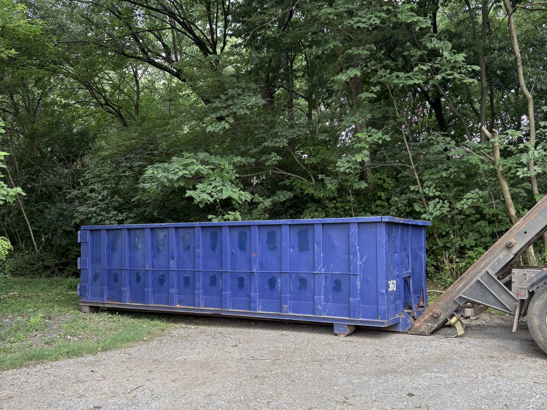 Blue roll-off dumpster placed on a wooded Maryland driveway