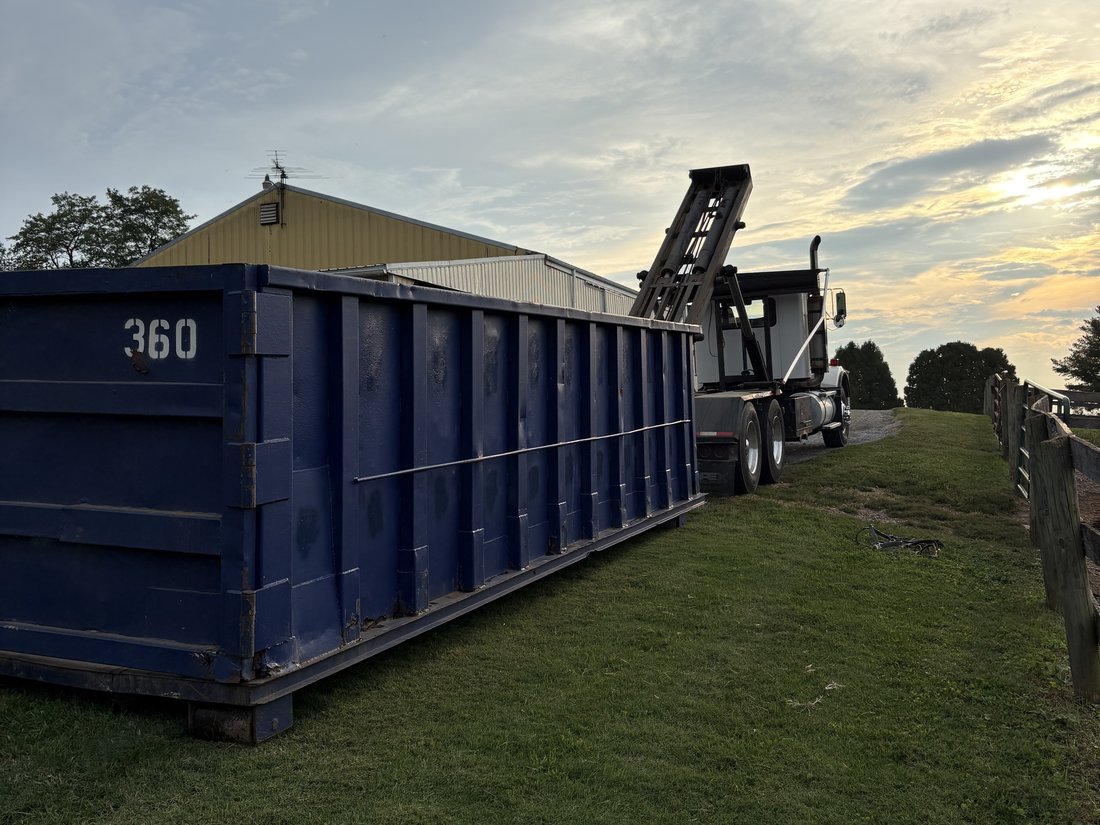 Blue roll-off dumpster delivered at a rural Maryland farm property at dusk